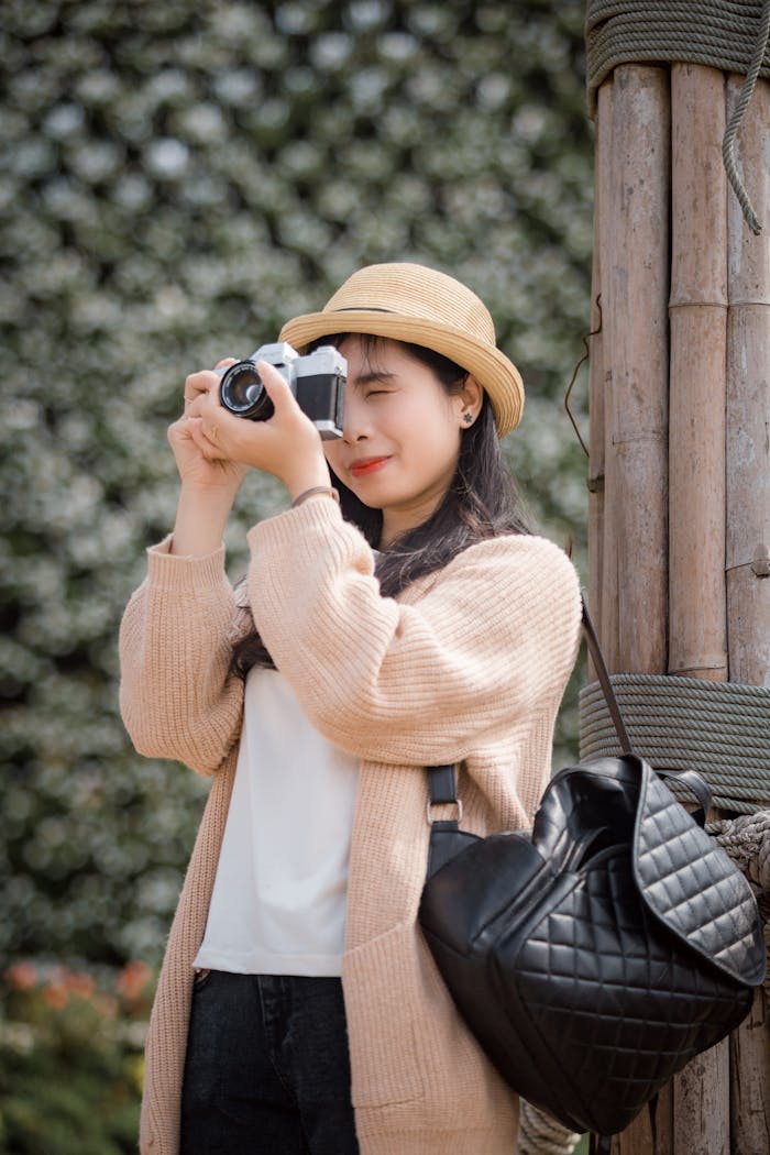 gallery-6 Asian woman in a hat taking photos with a vintage camera outdoors.