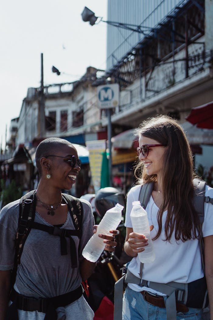 Two women enjoy a day out at a vibrant street market, holding water bottles and smiling.