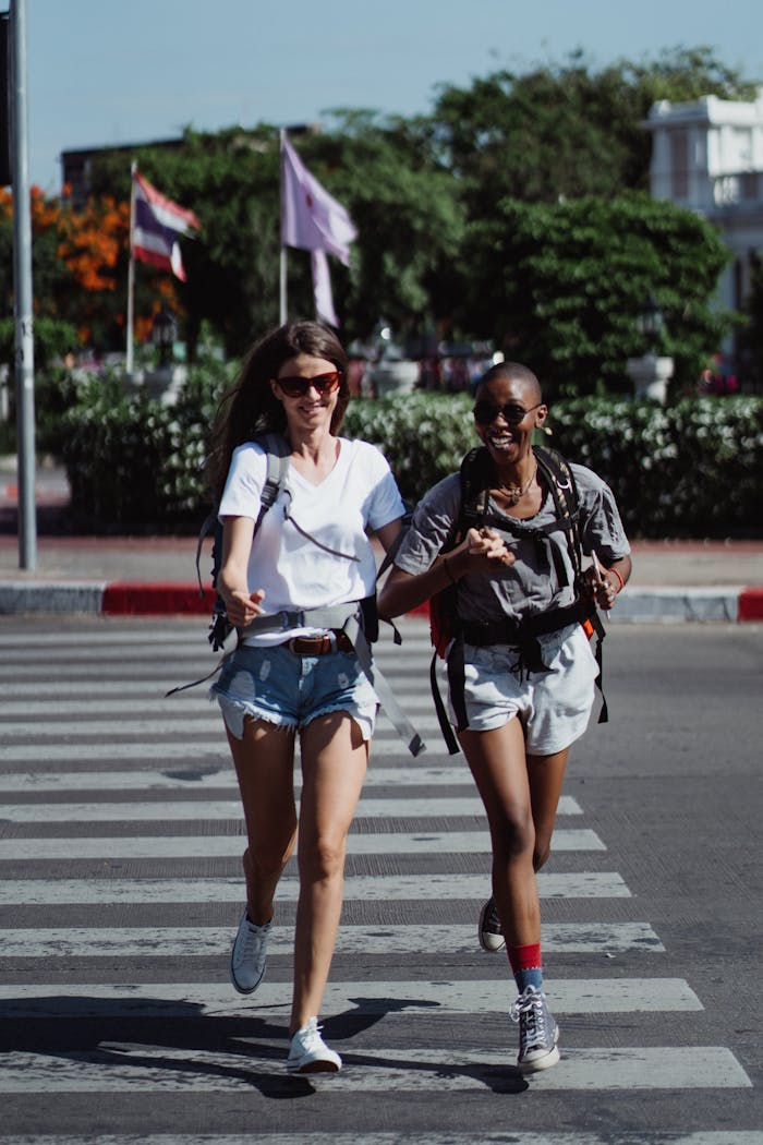 Two women laughing and running across a pedestrian crossing in a vibrant city setting.