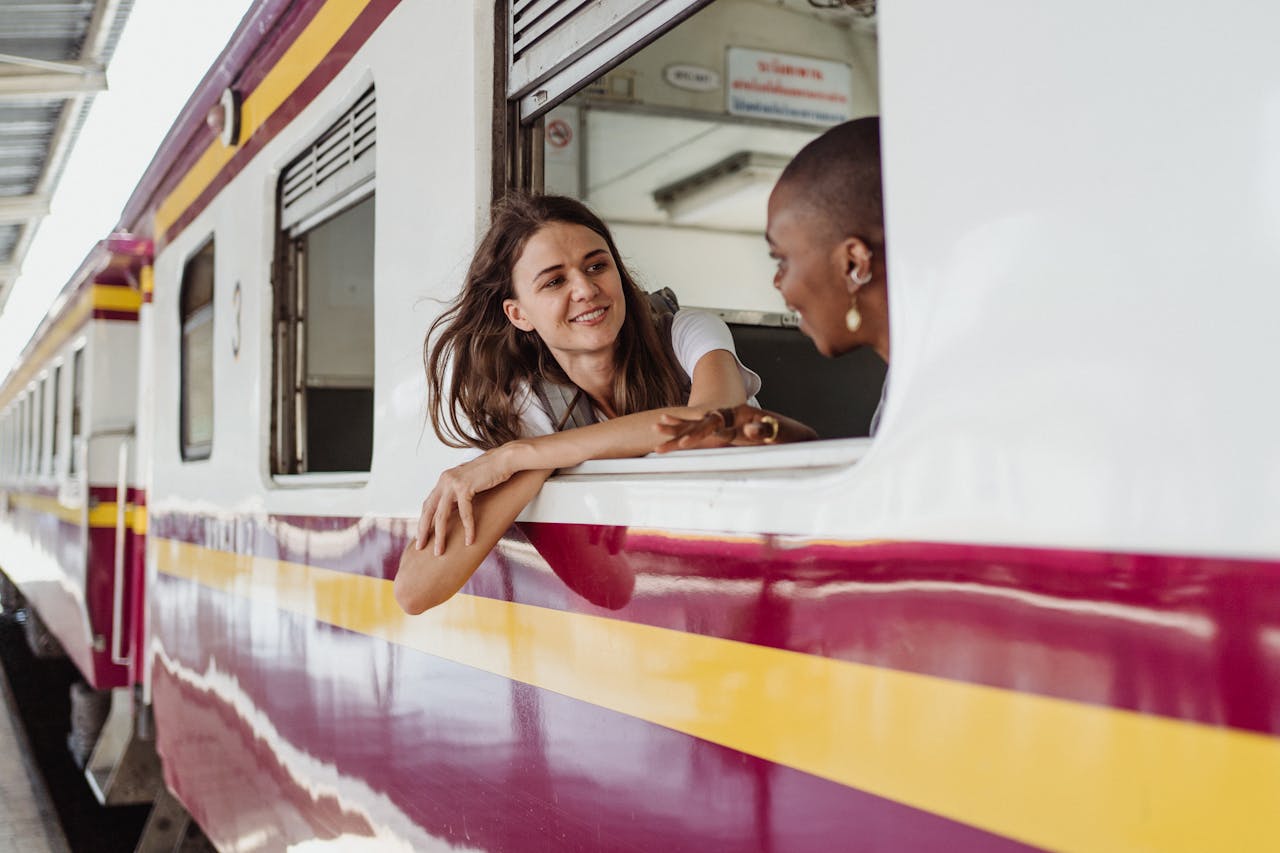 Two women enjoying a conversation while leaning out of a train window at a station.